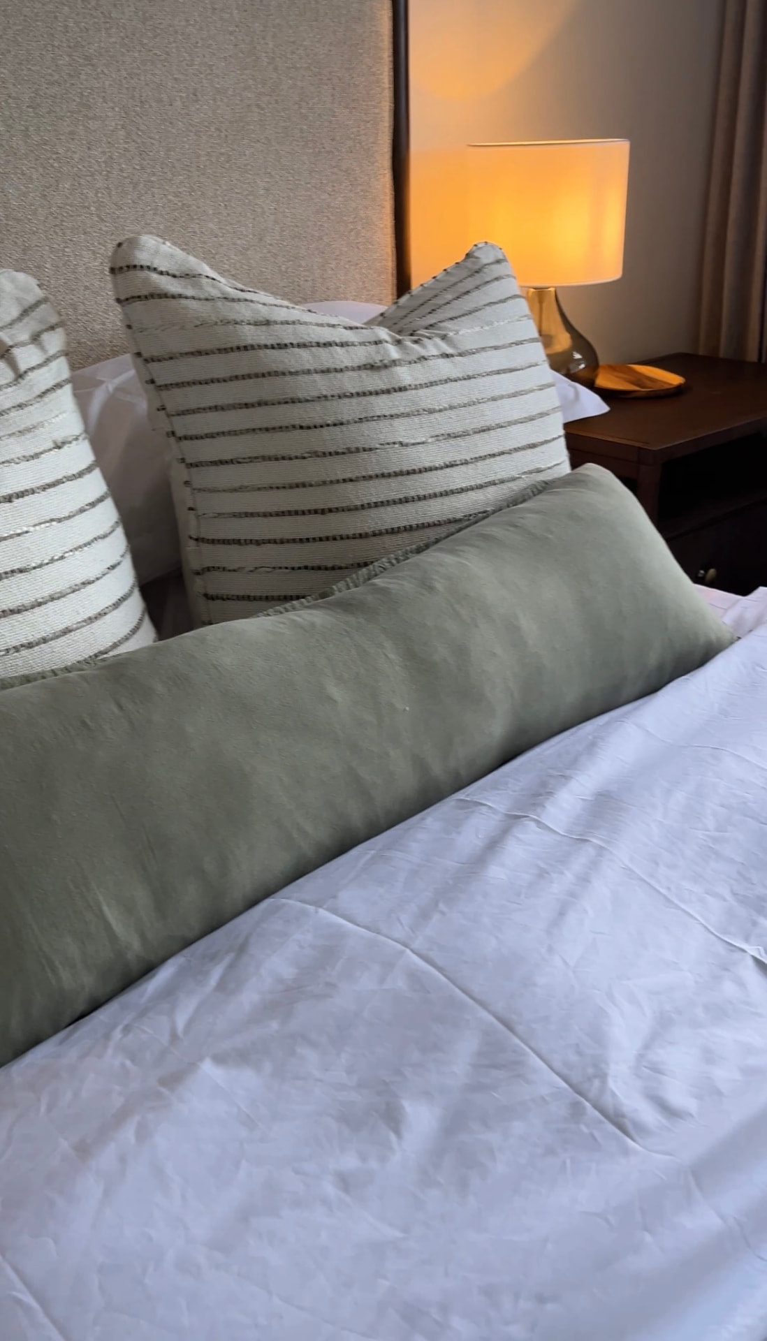 Sage bolster and striped cushions lit by a warm bedside lamp