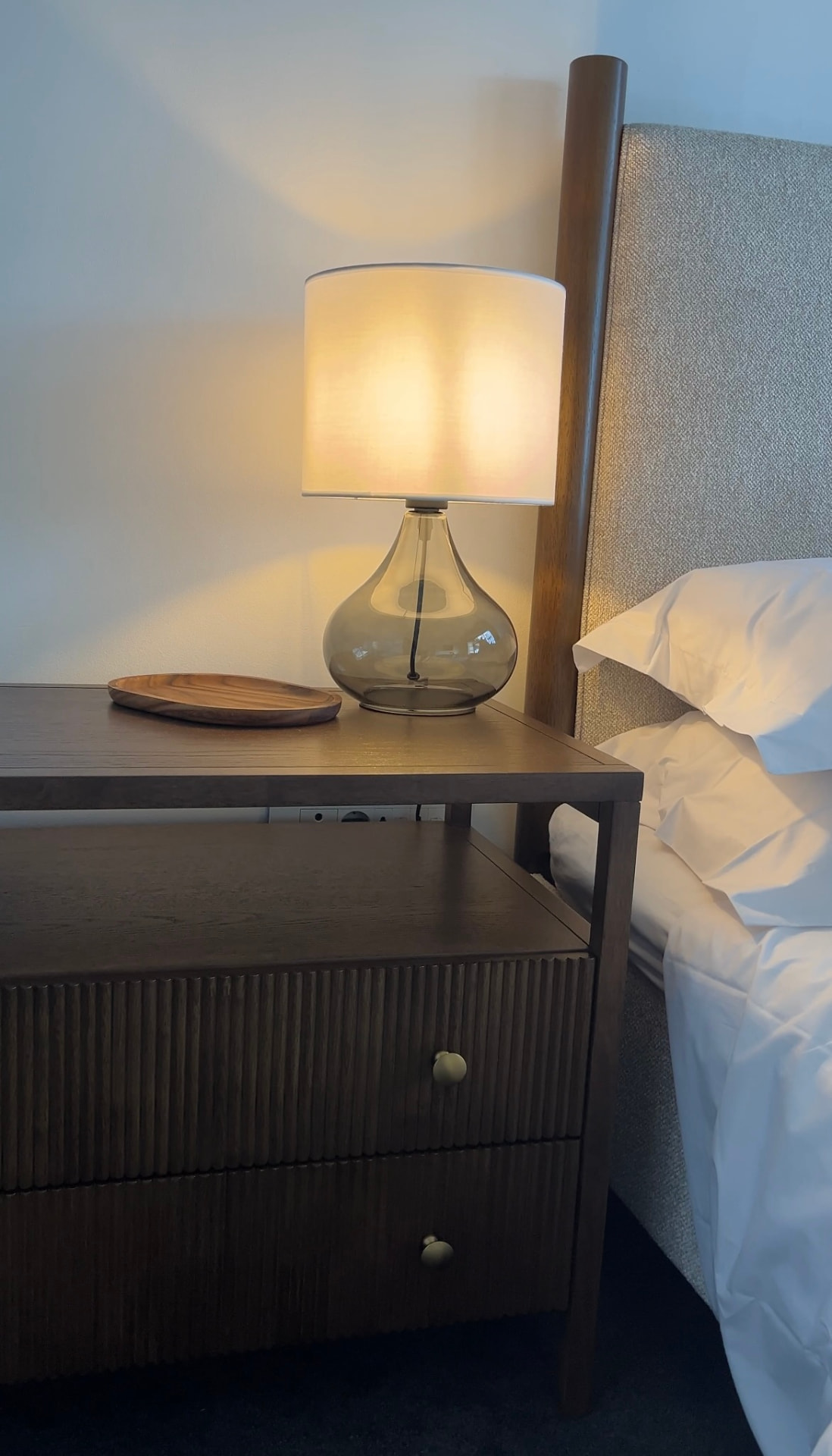 Glass table lamp and timber tray on a layered bedside setting