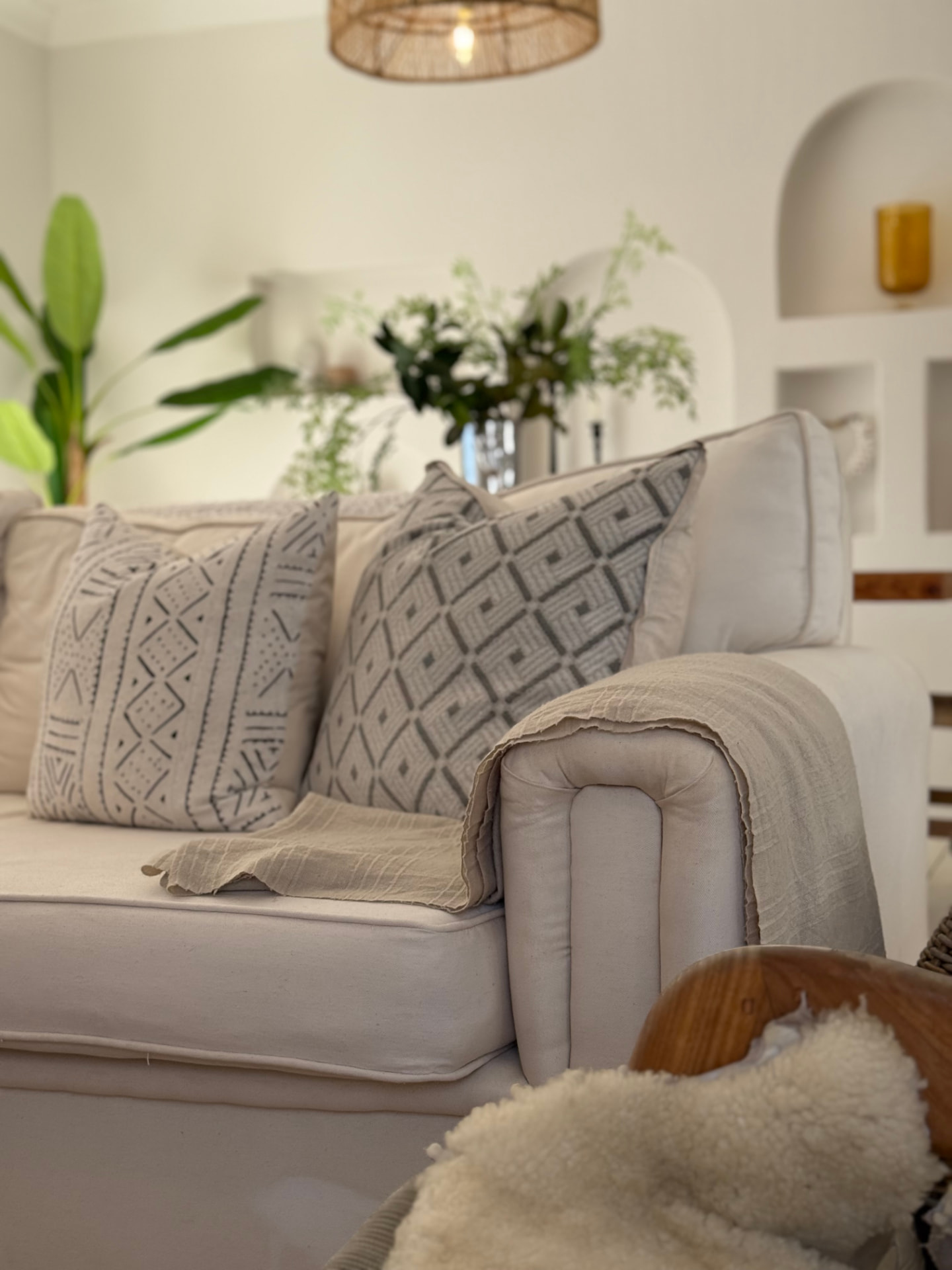 Linen sofa layered with mudcloth and woven cushions beside an arched plaster niche