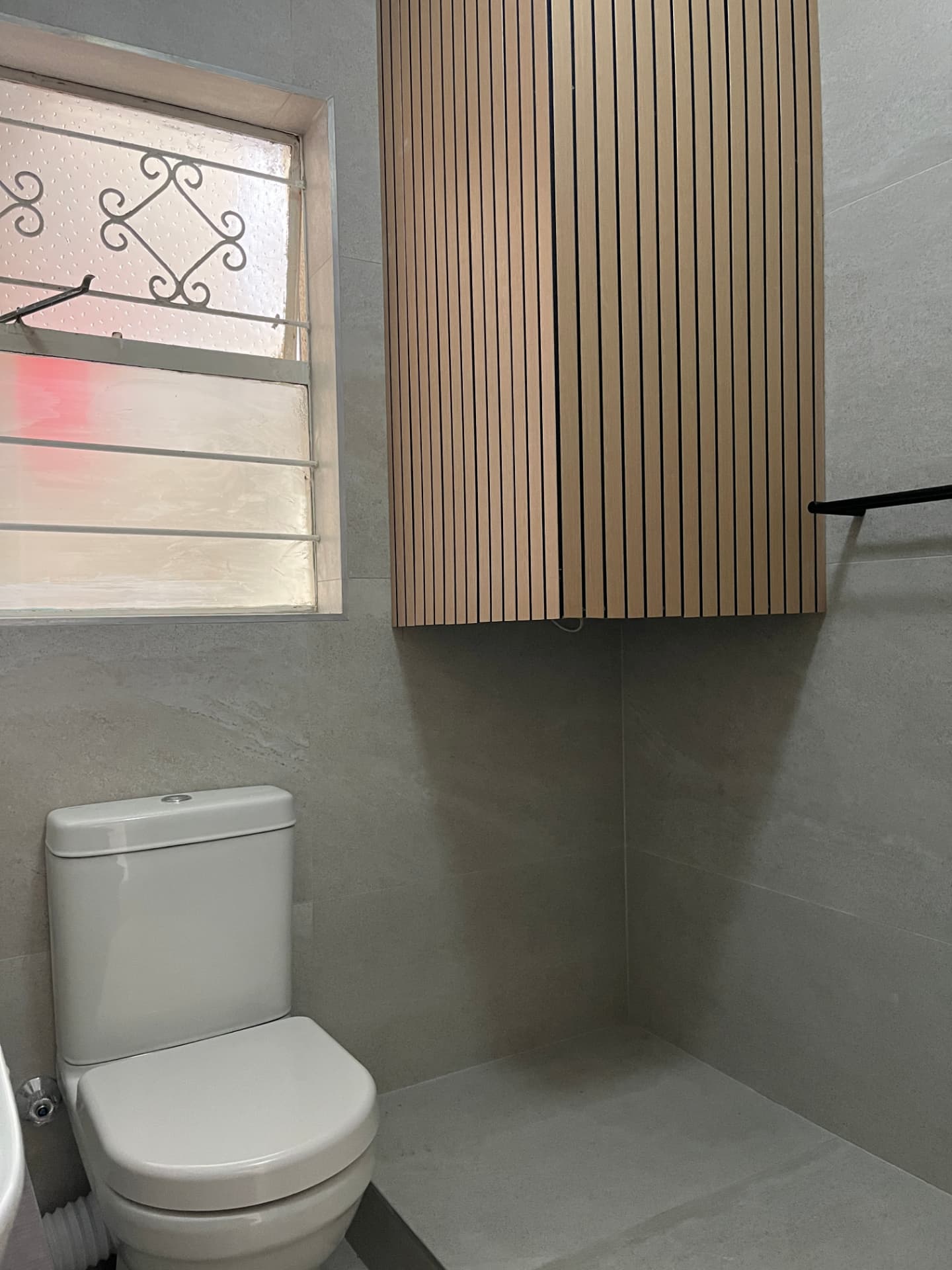 After: warm timber slatted cabinet beside the toilet in the finished bathroom
