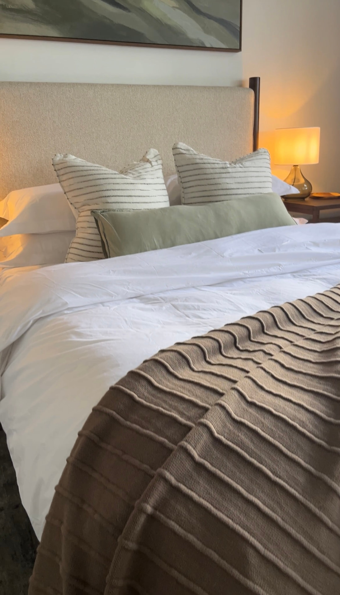 Bed dressed in white linen with a textured taupe throw and sage bolster