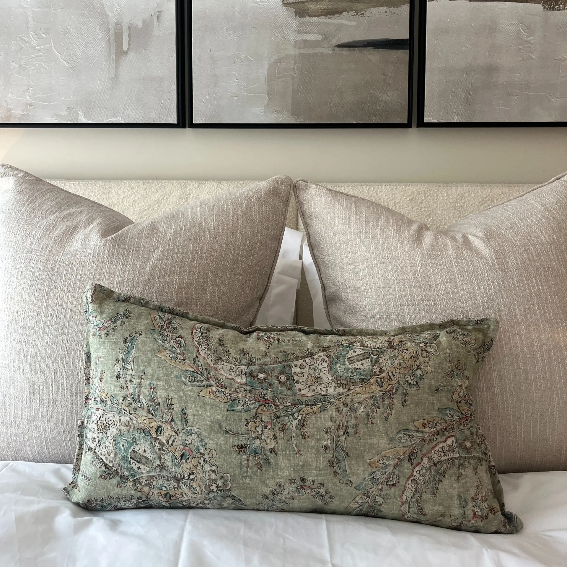 Detail of a green botanical print cushion against textured bed pillows