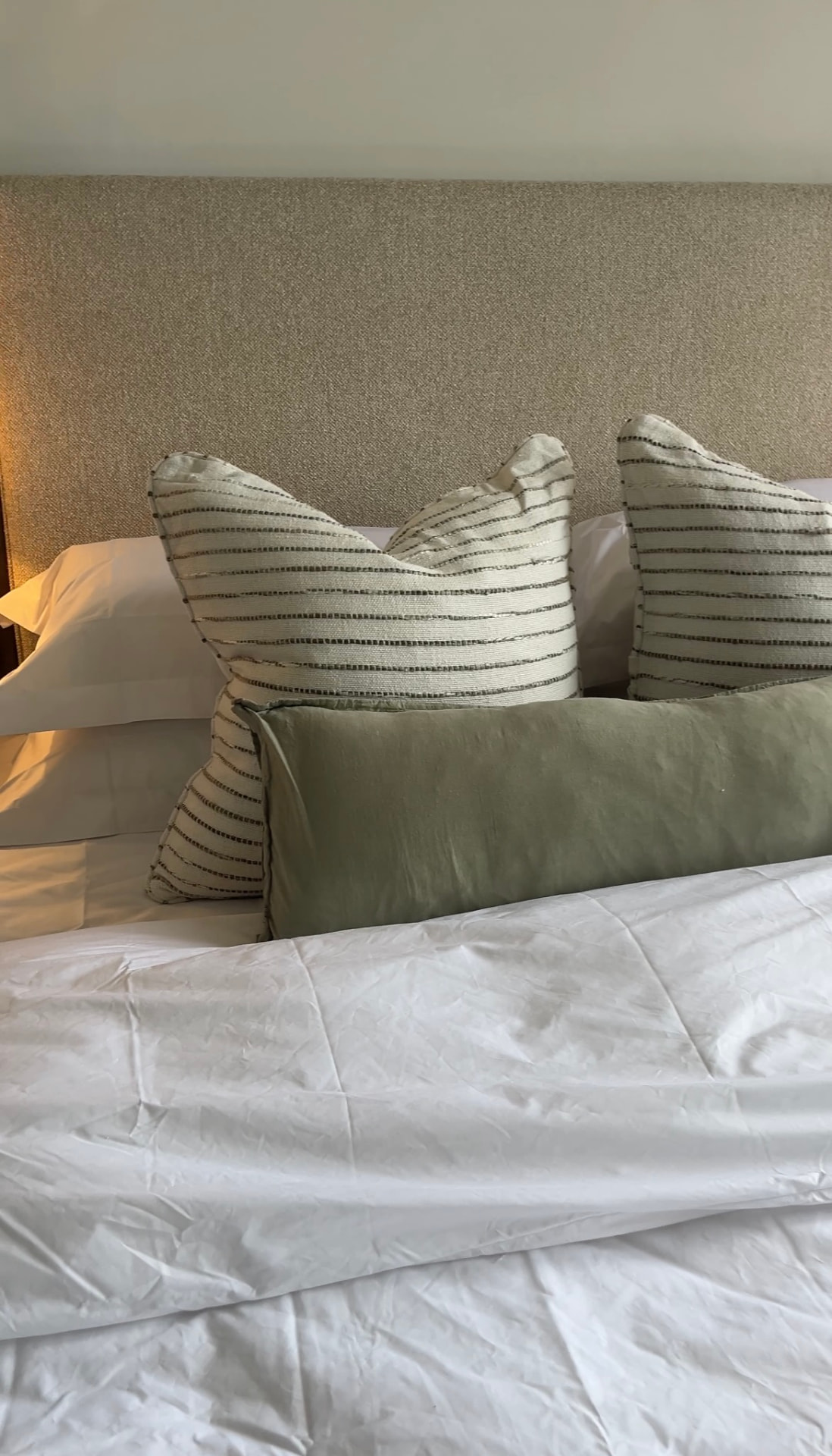 Striped scatter cushions and a sage linen bolster against a woven headboard