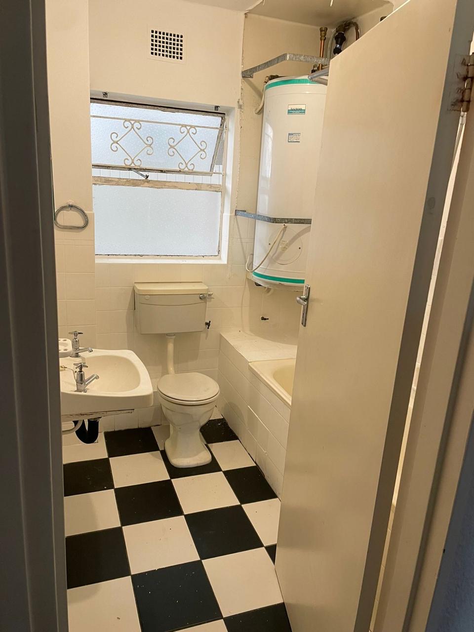 Before: original bathroom with checkerboard floor, exposed geyser and dated sanitaryware