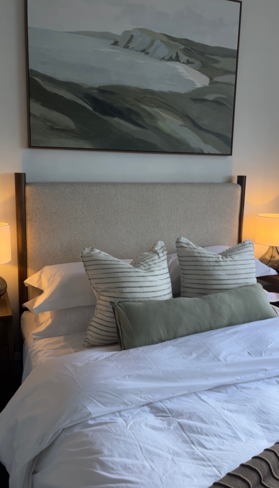 Bed with upholstered headboard beneath a soft green landscape artwork