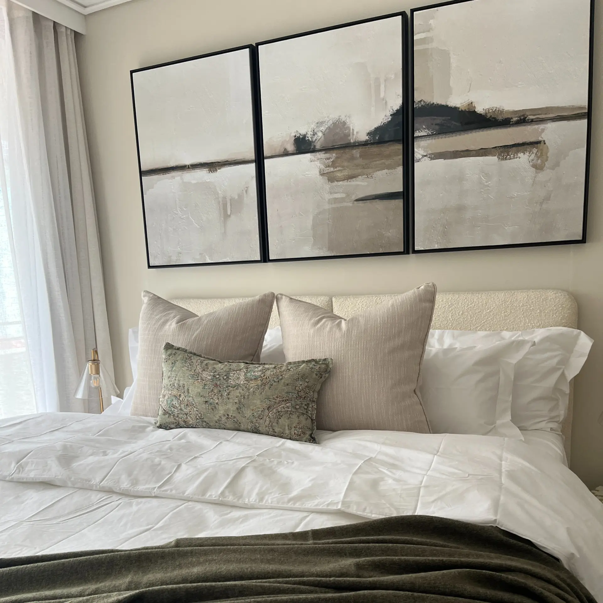 Bed dressed in white linen with an olive throw and printed cushion