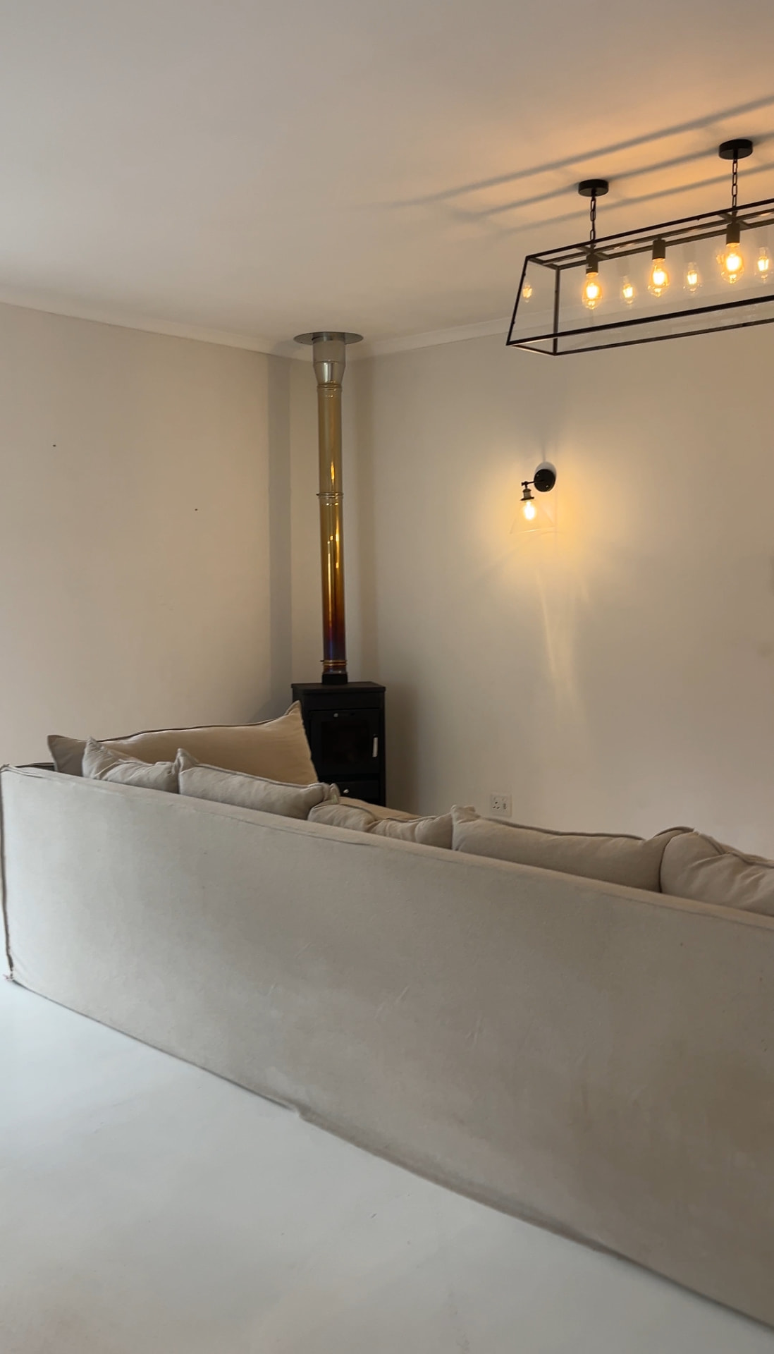 Living room with linen sofa, black wood-burning stove and lantern pendant
