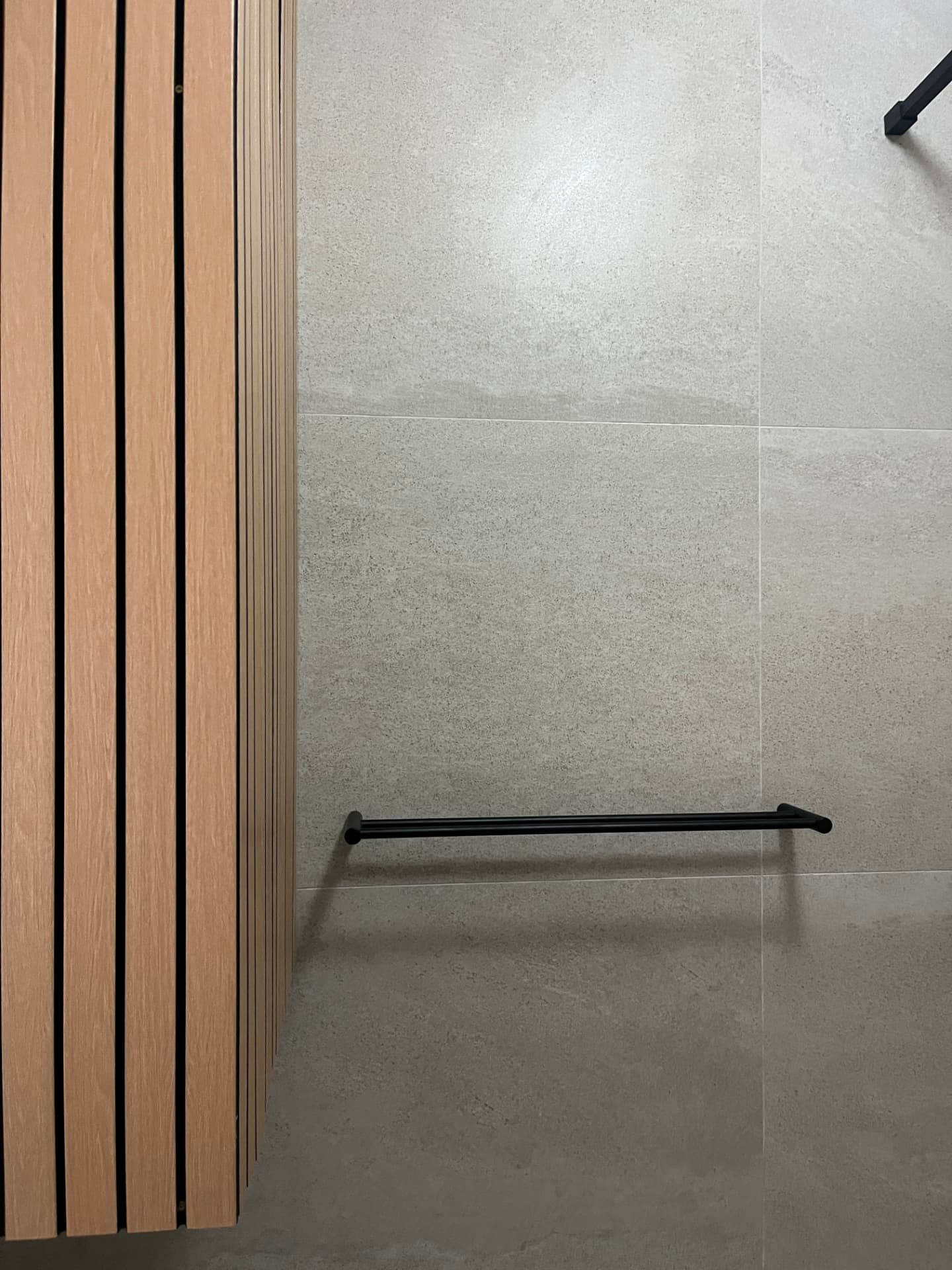 After: timber slat detail with matte black double towel rail on stone-look tile