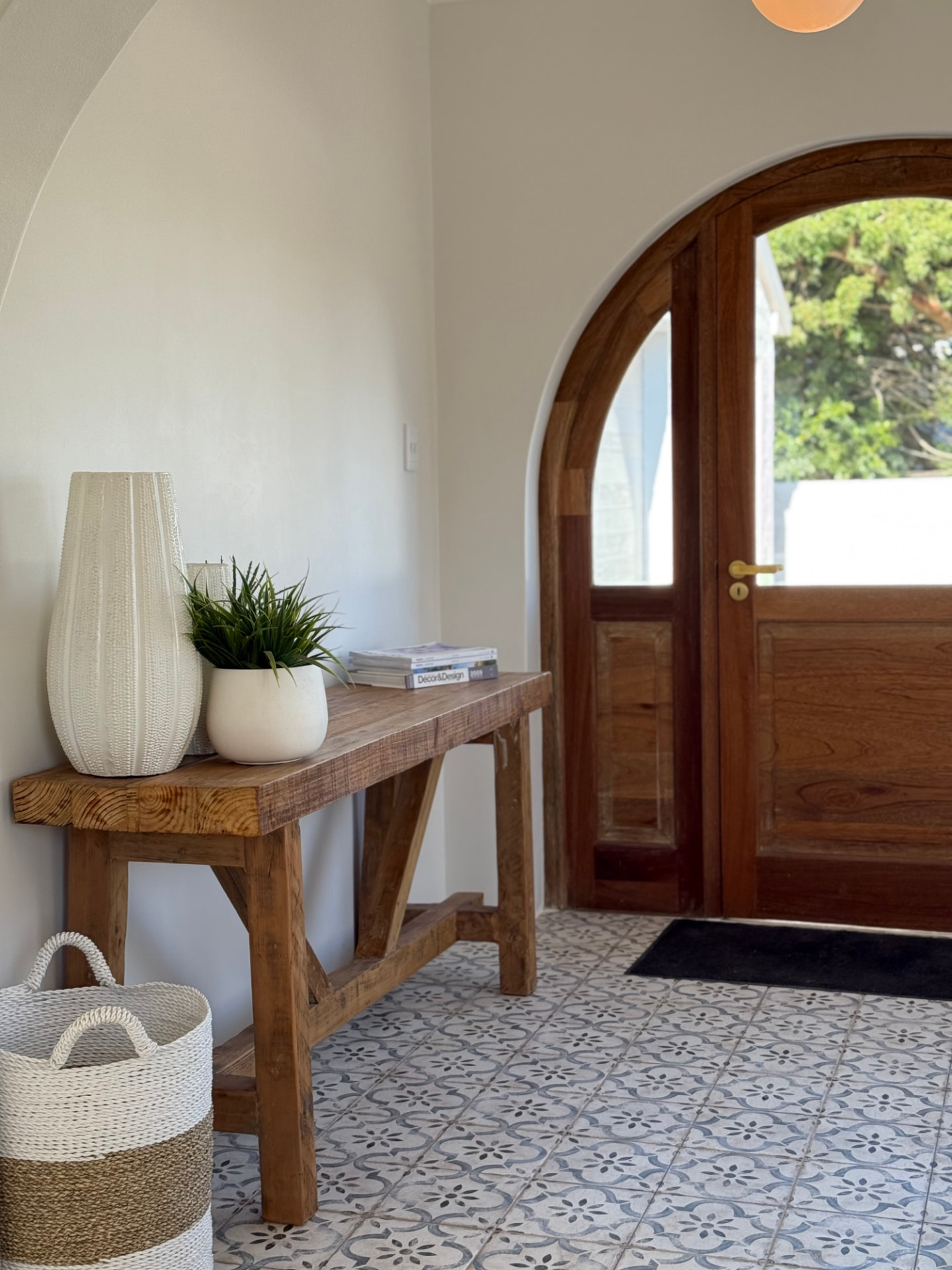Entrance hall with reclaimed timber console, ceramic vases and an arched timber front door