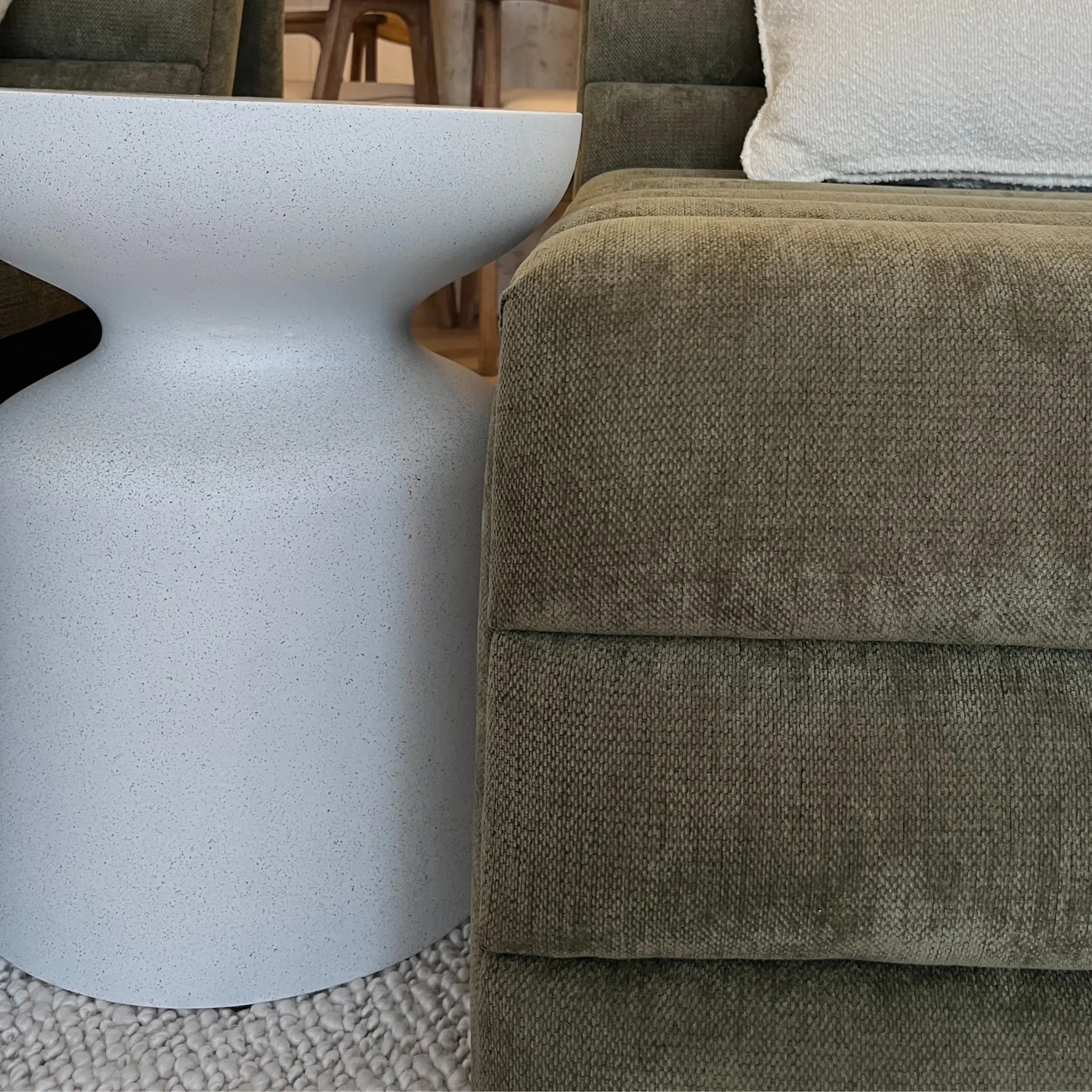 Speckled stone side table beside an olive chenille armchair