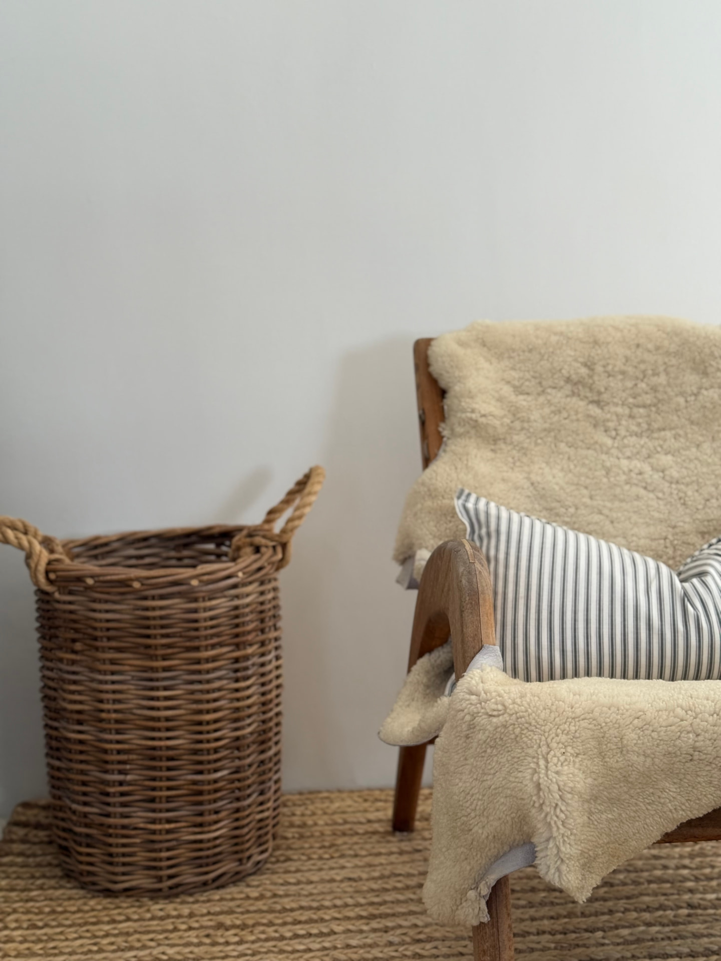 Timber armchair with sheepskin throw and ticking-stripe cushion on a jute rug