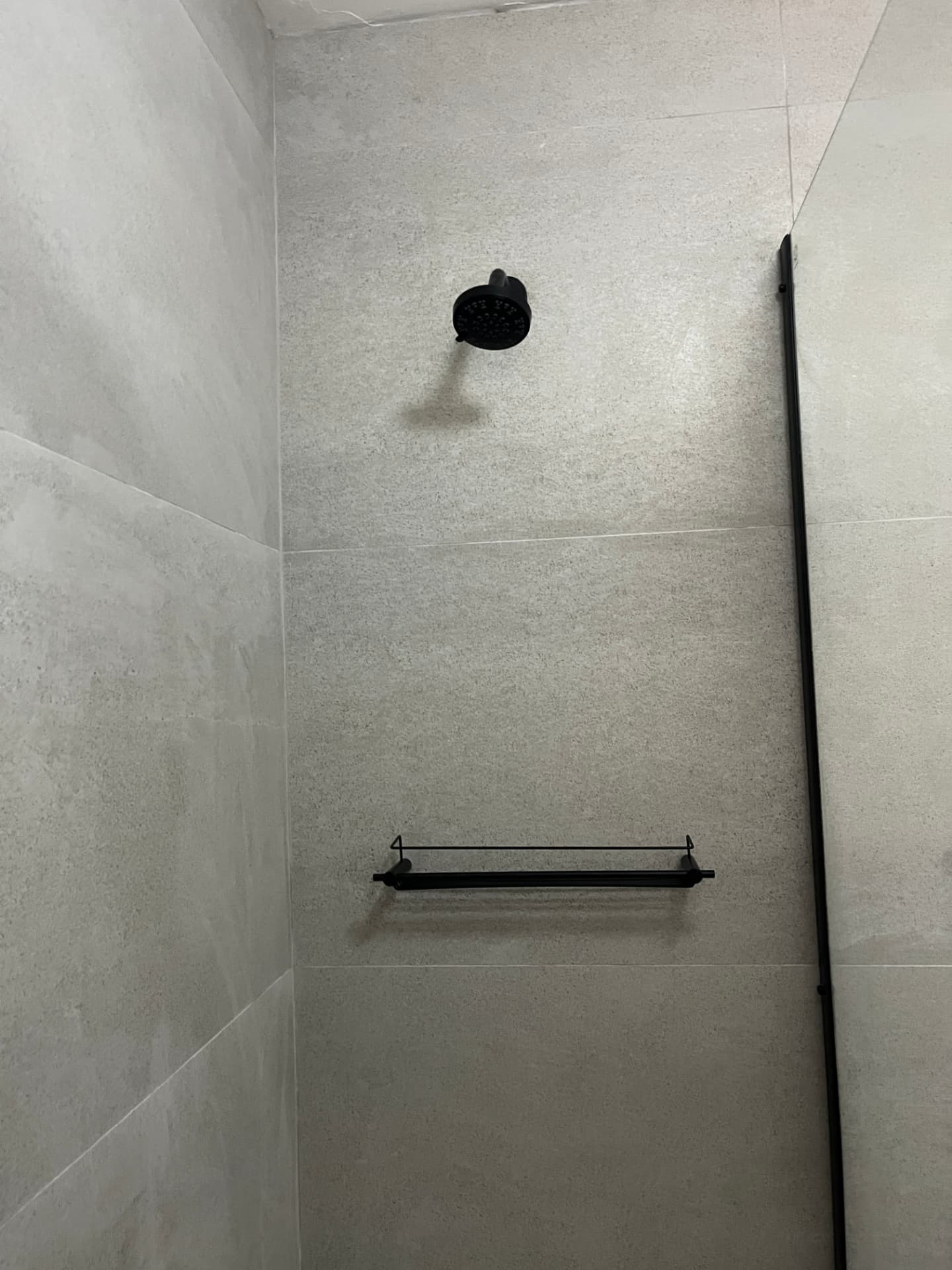 After: matte black shower head and shelf detail against stone-look porcelain tile